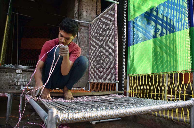 Skilled youngster knitting the traditional bed (Charpai) for sell at his workplace
