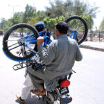 A pillion rider carrying a bicycle on a motorbike traveling on a busy road