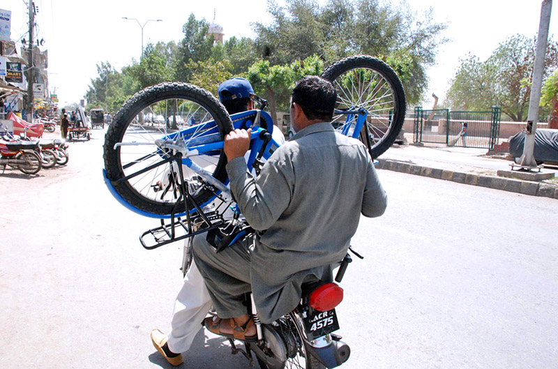 A pillion rider carrying a bicycle on a motorbike traveling on a busy road