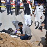 Police official inspect a dead body of a suspected attacker at the site of suicide attack on a convoy of foreign nationals in the Landhi area.