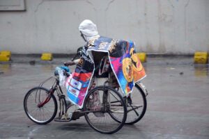 Elderly Special Person on his way during rain to protect himself with plastic sheet.