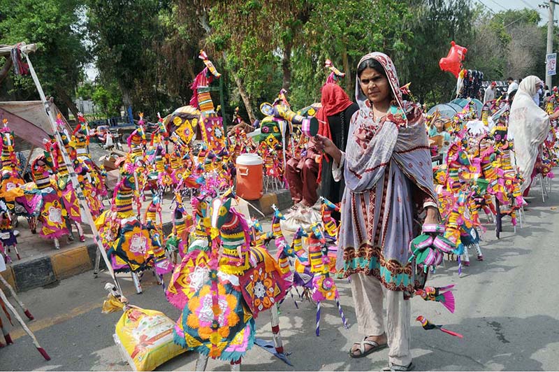 A gypsy woman vendor displaying and selling handmade toys for children at roadside setup to earn livelihood.