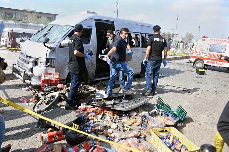 Police official inspect a dead body of a suspected attacker at the site of suicide attack on a convoy of foreign nationals in the Landhi area.