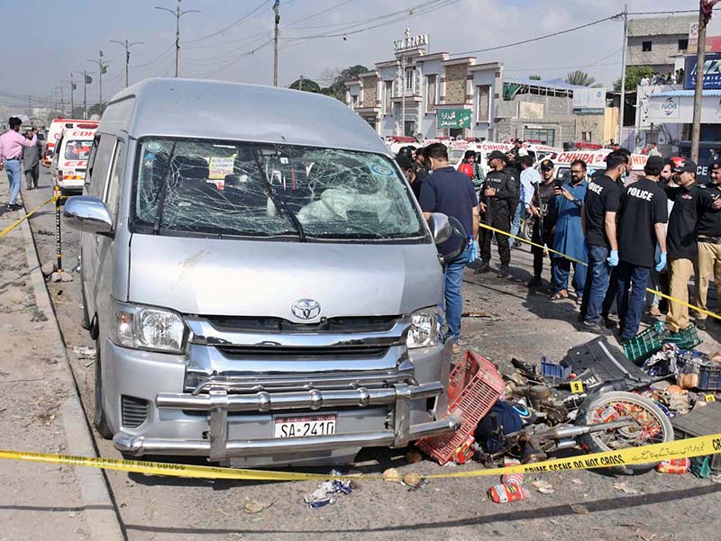 Police official inspect a dead body of a suspected attacker at the site of suicide attack on a convoy of foreign nationals in the Landhi area.