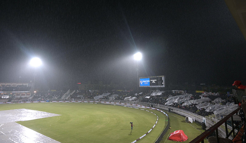 People sit under the cover of polythene sheet during rainfall before the start of the first Twenty20 International Cricket Match between Pakistan and New Zealand at the Rawalpindi Cricket Stadium