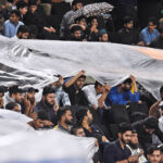 People sit under the cover of polythene sheet during rainfall before the start of the first Twenty20 International Cricket Match between Pakistan and New Zealand at the Rawalpindi Cricket Stadium