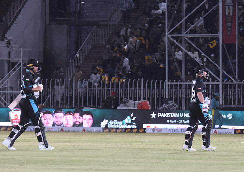 People sit under the cover of polythene sheet during rainfall before the start of the first Twenty20 International Cricket Match between Pakistan and New Zealand at the Rawalpindi Cricket Stadium