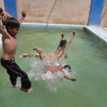 Youngsters jumping and bathing in the swimming pole to get relief from hot weather in the city.