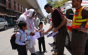 Rescue 1122 workers distributing heat stroke awareness pamphlets and water to a public at Stadium Chowk.