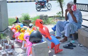 An elderly vendor displaying air filled plastic toys to attract the customers at his roadside setup.