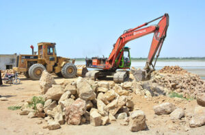 Labourers busy in repairing the embankment of Indus River with the help of machine at Husseinabad.