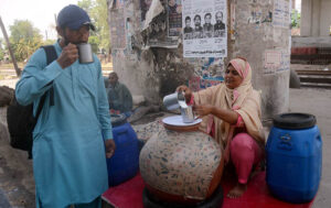 A Women Shopkeer drinking traditional summer drink (Lassi) from vendor to get relief from hot weather in the city