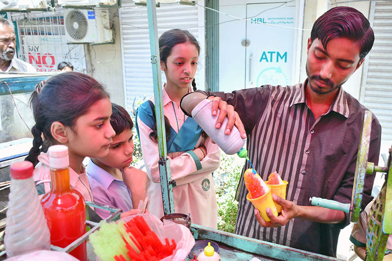 Students purchasing “gola ganda” (ice lolly) from vendor during hot weather in the city.