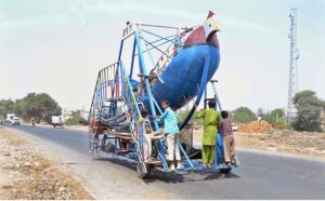 Vendor on the way with a swing boat heading towards the destination to earn livelihood while children standing on swing that may cause mishap due to improper safety equipments.