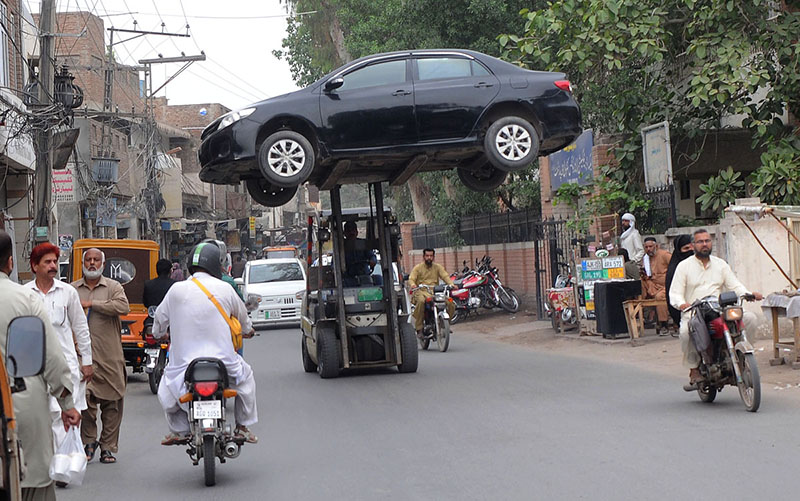 Traffic warden removing the wrong parked car with the help of a forklift in front of the excise office for the smooth flow of traffic near MDA Chowk.