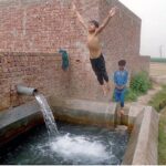 Youngsters bathing in tube well to get some relief from hot weather in the city
