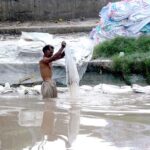 A man washing plastic sacks in local canal for resell