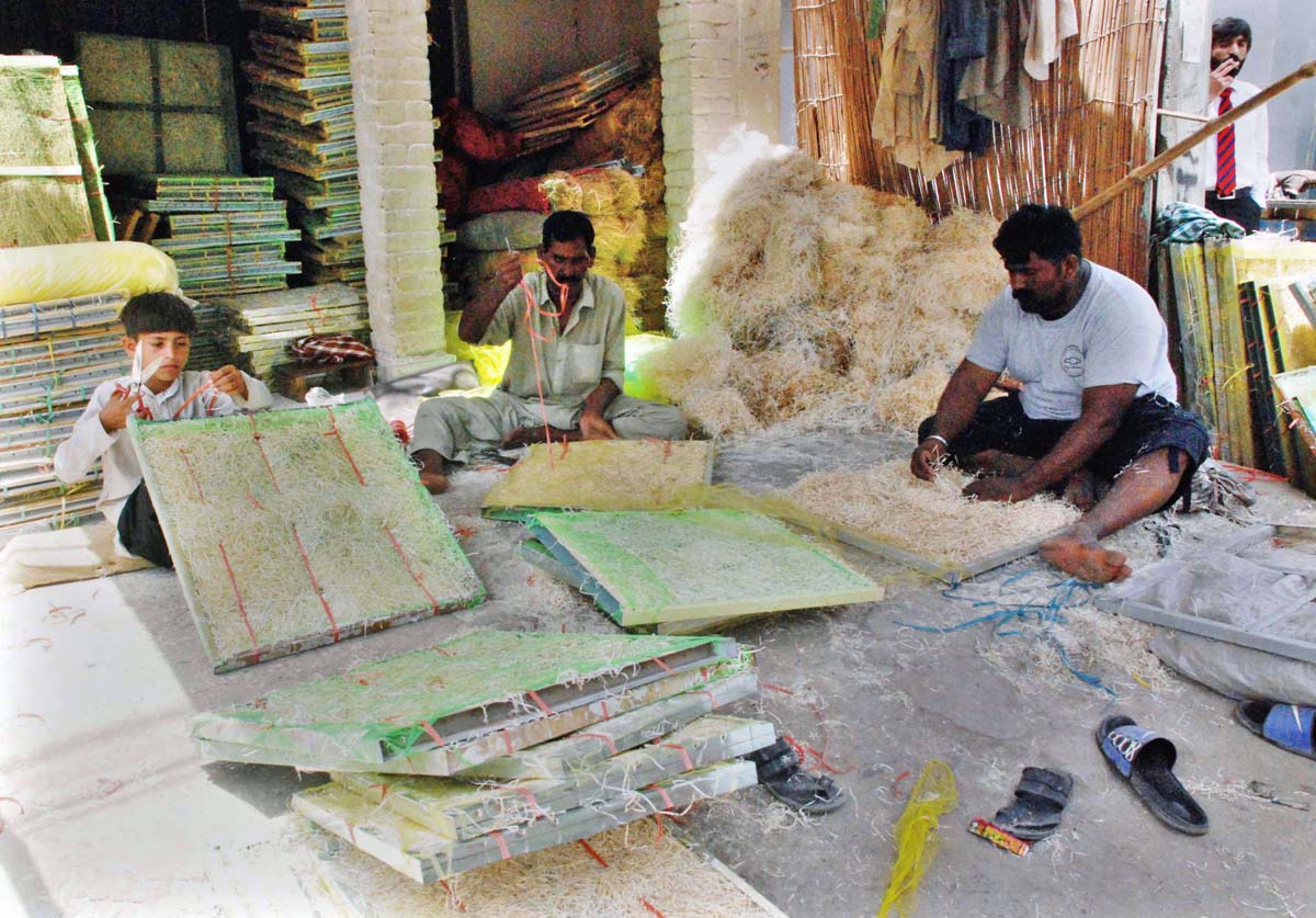 Workers are busy filling husk in frames of air coolers at their workplace.