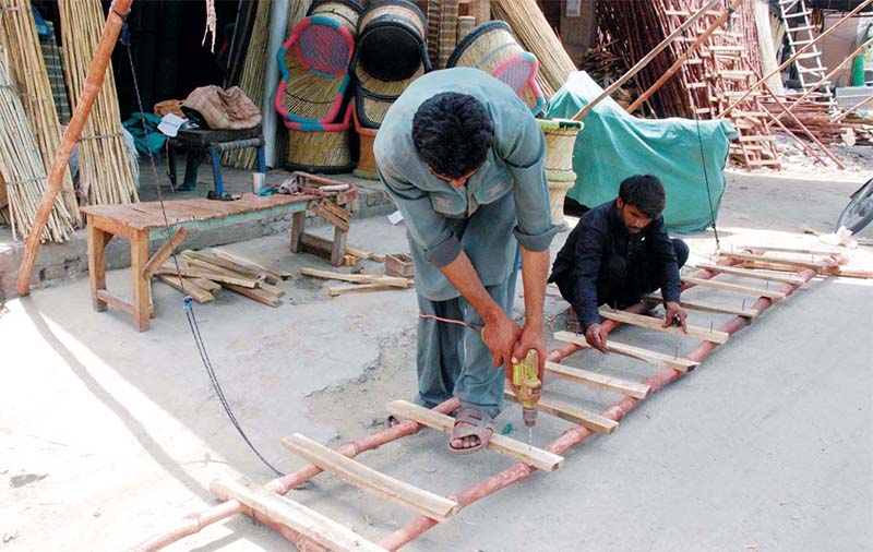 Two workers build a ladder by the side of the road using bamboo and wood.