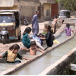 Children bathing in the channel of tub-well to get relief from scorching hot weather in the city