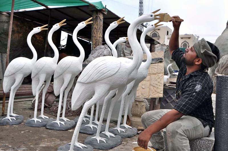 A painter giving final touch to statue of bird at his workplace.