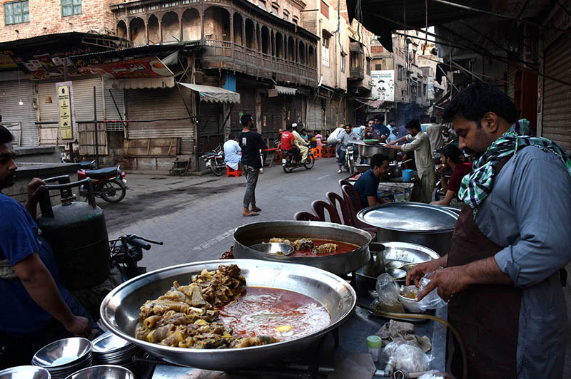 A vendor selling the traditional food (Siri Paaye) as People eat the different kind of traditional breakfast at a food stalls alongside a road in the old city (walled city) inside the dehli gate in early morning.