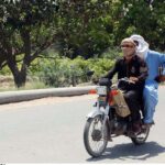 Due to the extreme heat, people are traveling on a motorcycle by covering their face with cloth handkerchiefs.