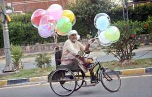 A disable vendor on the way on wheelchair tricycle selling balloons to earn livelihood.