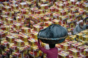 Labourer carrying the vegetable basket on his head as in the background a peach boxes arranging after unloaded from delivery truck at Vegetable and Fruit Market.