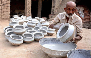 Worker busy in coloring on the clay made pots at his workplace.