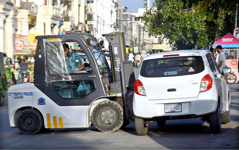 Traffic warden removing the wrong parked car with the help of a forklift in front of the excise office for the smooth flow of traffic at Mall Road