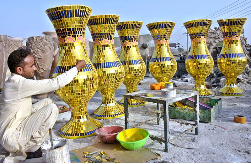 An artist is engaged in finalizing a household decorative vase by applying his artistic skills of glazing and Parchinkari on pottery.