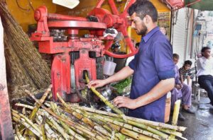 A vendor is extracting sugarcane juice with the help of machine to attract customers at his shop.