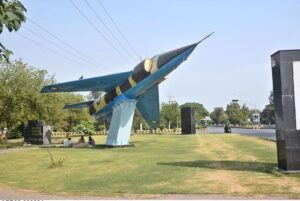 People sitting under the shadow of fighter plane model installed at roadside greenbelt in I-9 Sector during scorching hot weather in Federal Capital.