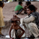 A Gypsy father carefully cuts his son's hair at their roadside temporary home