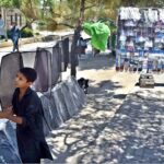 A young vendor arranging and displaying car sun shades to attract the customers along Murree Road