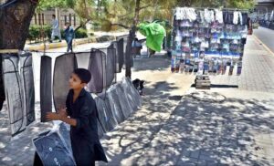 A young vendor arranging and displaying car sun shades to attract the customers along Murree Road