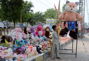 A young vendor arranging and displaying toys on footpath to attract the customers.