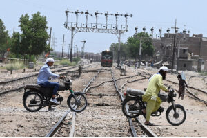 Motorcyclists crossing railway track while train approaching on the same track near railway station.