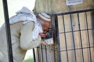 Elder man drinking water from water cooler to crunch their thirst during hot weather in the city.