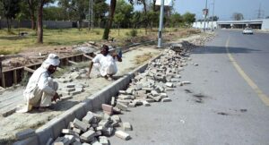 Labourers busy in fixing cemented tiles on footpath along Park Road in Federal Capital.