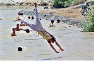 A young boy diving into a canal water to escape the city's scorching heat .