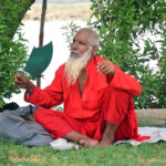 An elderly man fanning himself with a hand fan at green belt during the scorching weather in the city