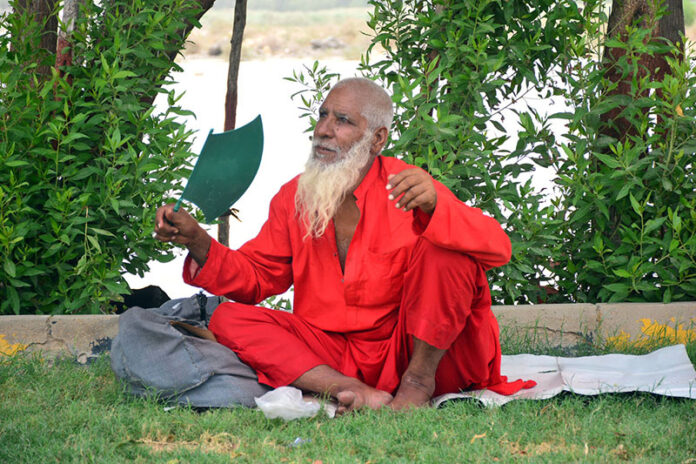 An elderly man fanning himself with a hand fan at green belt during the scorching weather in the city