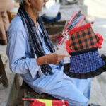 An elder vendor sells hand fans at roadside during hot day in the city
