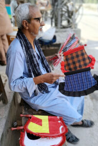 An elder vendor sells hand fans at roadside during hot day in the city