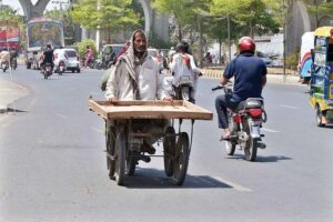 A person carrying a hand cart while sitting on the rear seat of the motorcycle on the way at a General Bus stand road.