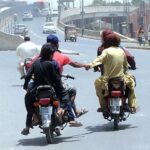 A pillion rider holding the hand of another motorcyclist, heading towards a petrol pump for refueling