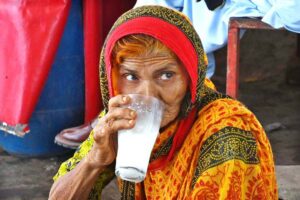 An elderly woman drinking traditional drink (lassi) from the vendor at Bacha Khan Chowk during hot weather in the city.