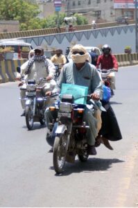 A pillion rider holding the hand of another motorcyclist, heading towards a petrol pump for refueling